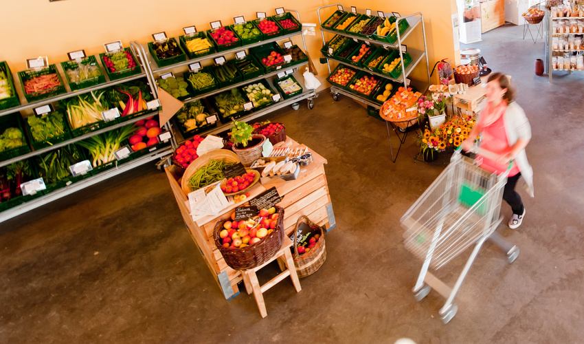 KI generiert: Ein Laden mit frischem Obst und Gemüse, eine Person schiebt einen Einkaufswagen.