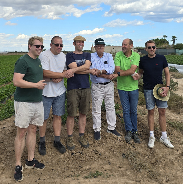 KI generiert: Eine Gruppe von sechs Männern steht auf einem Feld unter einem leicht bewölkten Himmel. Die Stimmung wirkt freundlich und entspannt in einer ländlichen Umgebung.